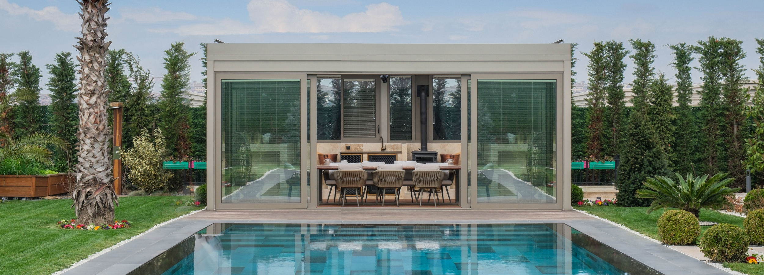 Retractable louvered aluminum pergola with integrated glass walls beside a pool, showcasing modern outdoor living and luxury design.